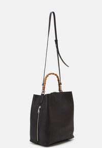 Borsa tote nera in pelle con finitura testurizzata, manico in bambù e tracolla removibile; presenta una zip argentata su un lato.