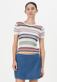 Stripet strikket kortermet topp med forskjellige farger på en kremfarget bakgrunn; kombinert med et blått denimskjørt, glatt tekstur, tettsittende design.