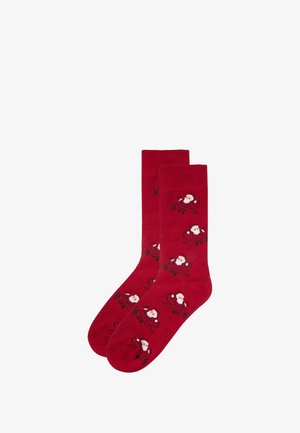 Rote Baumwollsocken mit einem Muster von Santa Claus im Flugzeug. Die Socken sind am oberen Ende gerippt, haben eine glatte Textur und eine abgerundete Zehenpartie.
