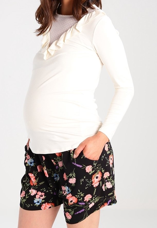 Top crema a maniche lunghe con scollatura arricciata abbinato a pantaloni corti neri a fiori con fiori rosa e blu.