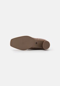 Suela de zapato de cuero marrón con punta cuadrada y tacón redondo, mostrando patrones y el texto "ANTI SLIDE" en el tacón.