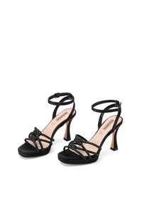 Sandali neri con tacchi a spillo, punta quadrata e più cinturini intrecciati. Tacco a stiletto con un accento a contrasto color tan e una superficie texture.