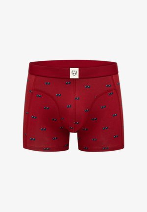 Bóxers rojos de hombre con pequeños estampados dispersos de gafas de sol azules y una etiqueta blanca con un logo de león negro en la cintura.