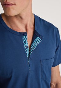Donkerblauwe shirt met een gestructureerde voorpanden met blauwe en turquoise stippenpatronen. Inclusief een zak en twee knopen bij de kraag.