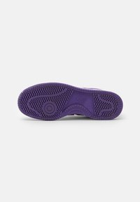 Fioletowa gumowa podeszwa sneakersów z teksturowanym wzorem bieżnika i okrągłym elementem designu. Posiada wytłoczone logo New Balance na boku.