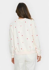 Krämsfärgad sweatshirt med röda hjärtstryktningar, ribbade muddar och fåll. Mjuk tyg, avslappnad passform och rundad halsringning.