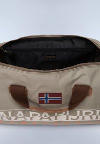 Borsa da viaggio in tessuto beige con manici marroni, con una patch a forma di bandiera norvegese e un interno nero dotato di tasca con zip.
