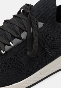 Schwarze gestrickte Sneakers mit strukturiertem Obermaterial, flachen Schnürsenkeln und glänzenden schwarzen Akzenten. Verfügt über eine strukturierte Sohle und eine neutralfarbene Zwischensohle.