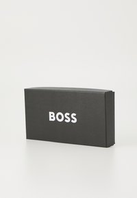Zwarte rechthoekige doos met afgeronde hoeken. Witte "BOSS" logo op de voorkant, gladde matte textuur, minimalistisch ontwerp.