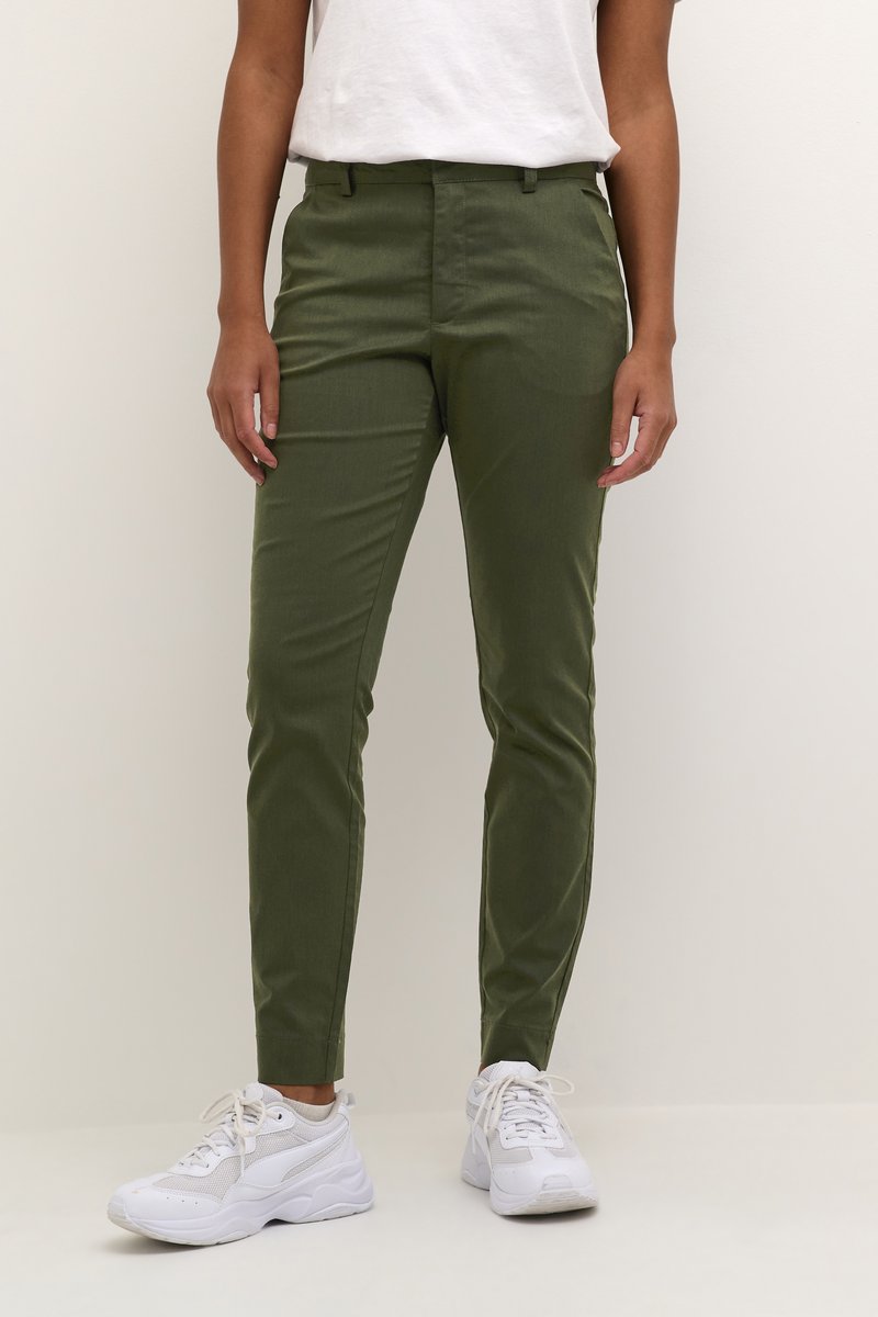 Pantalones ajustados verdes con una textura suave, con una cinturilla de altura media, bolsillos laterales y un corte de tobillo ajustado, combinados con zapatillas blancas.