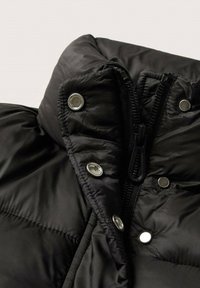 Collo del giubbotto imbottito nero con una finitura lucida, dotato di chiusura con zip, bottoni a pressione e texture trapuntata per isolamento.
