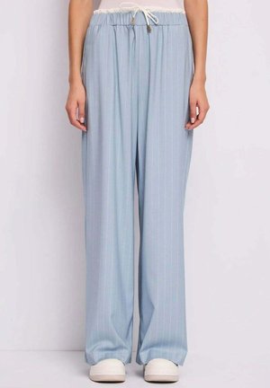 Donna che indossa pantaloni a righe sottili azzurri a gamba larga con vita elastica e coulisse bianca, abbinati a sneakers bianche.