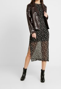 Svart blommig klänning med en genomsynlig överdel, sidoklipp, kombinerad med en mörkbrun läderbikerjacka och svarta ankelstövlar.