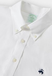 Witte katoenen shirt met een kraag met knopen, voorzien van twee knoopsluitingen en een marineblauw geborduurd logo van een beer op de linkerborst.