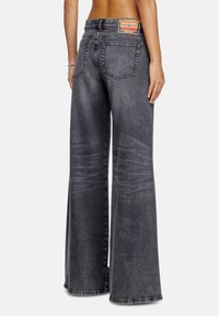 Jean en denim gris foncé à jambe large avec une texture délavée, des coutures accentuées et une étiquette en cuir de marque sur la taille.