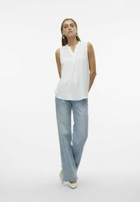 Haut blanc sans manches avec un décolleté en V et une coupe décontractée, associé à un jean bleu clair à jambes larges et des escarpins blancs à bout pointu. Design simple et texturé.