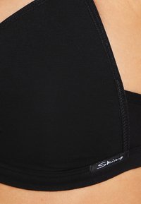 Zwarte bralette van ribstof, met een driehoekige cupvorm en zachte randen. Inclusief een klein label met de merknaam.