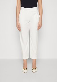 Pantaloni bianchi su misura a gamba dritta, caratterizzati da una texture liscia e tasche laterali, abbinati a scarpe con punta a becco con dettagli dorati.