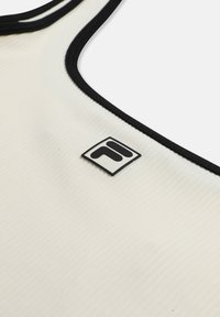 Primer plano de una prenda de tela blanca acanalada con ribete negro y un pequeño parche de logotipo en blanco y negro cerca del escote.