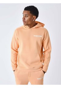 Sudadera color durazno con bolsillo canguro, capucha con cordones y texto del logo en blanco. Tejido suave y puños acanalados, combinada con joggers a juego.