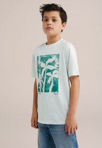 T-shirt di cotone azzurro chiaro con grafica di una palma verde e testo al centro. Maniche corte e scollatura rotonda. Vestibilità casual.