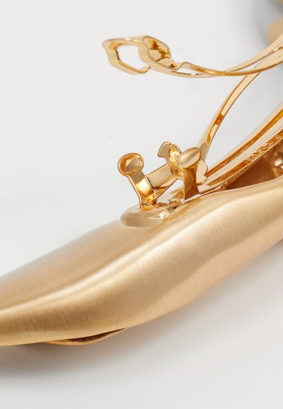 Gouden schoen met een gladde metallische afwerking, voorzien van intrigerende decoratieve accenten en een gebogen silhouet voor een elegante uitstraling.