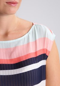 Maglietta leggera a righe nei colori pastello: blu chiaro, rosa corallo e blu navy. Presenta una trama traslucida con maniche corte e scollatura rotonda.