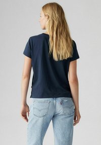 Una camiseta de manga corta azul marino hecha de una tela suave, combinada con unos vaqueros de mezclilla azul claro que tienen bolsillos traseros y detalles de costura.
