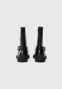 Black leather ankle boots with a smooth finish, featuring a prominent buckle detail, structured design, and chunky rubber soles.