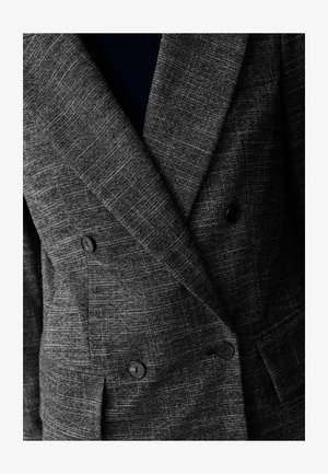Giacca grigia texturizzata a doppio petto con motivo a sottile houndstooth, bottoni neri e rever larghi. Strato interno visibile in blu scuro.