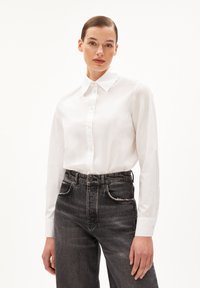 Camicia bianca con bottoni, realizzata in cotone; presenta un colletto classico e maniche lunghe. Abbinata a jeans grigio scuro a vita alta con tasche.