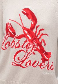 Suéter de punto beige con un gráfico detallado de una langosta roja y texto en cursiva roja que dice "Amantes de las Langostas" en el frente.