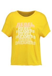 Žluté bavlněné tričko s volným střihem a kulatým výstřihem. Na přední straně je vytištěn výrazný nápis "REBEL DREAMERS" v různých barvách.