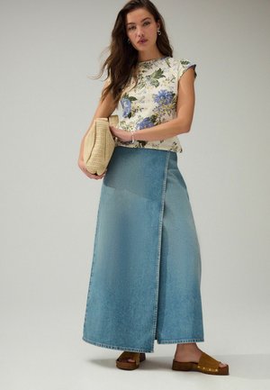 Haut à imprimé floral à manches courtes ; jupe en denim bleu clair avec une fente à l'avant ; sandales en suède marron ; sac en toile tissé.