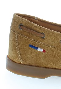 Zapato casual de ante marrón con suela de goma, que presenta un pequeño acento bordado en rojo, blanco y azul, así como detalles de cordones de cuero.