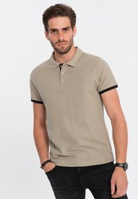 Khaki polo tričko s krátkým rukávem, černými akcenty na rukávech, tříknoflíkovou légou a hladkou bavlněnou směsovou texturou.