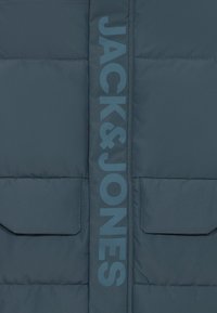 Geacă matlasată albastru închis, cu logo-ul vertical "JACK & JONES", două buzunare frontale și textură matlasată. Finisaj mat predominant.