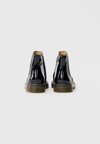 Bottines en cuir verni noir avec une texture lisse, bout arrondi et semelle robuste. Fermetures éclair décoratives sur le côté et couture contrastée visibles.