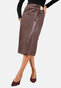 Gonna a matita in pelle marrone con design avvolgente frontale e chiusura laterale. Texture liscia, lunghezza al ginocchio, abbinata a tacchi bordeaux.