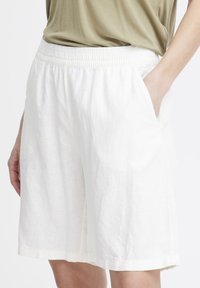 Un short en lin blanc avec une taille élastique et des poches latérales, fabriqué dans un tissu léger et texturé pour la respirabilité et le confort.