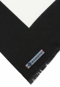 Schwarz-weißer Schal mit solidem schwarzen Rand und weißer Mitte, fransigen Kanten und einem grauen Etikett mit roten Akzenten.