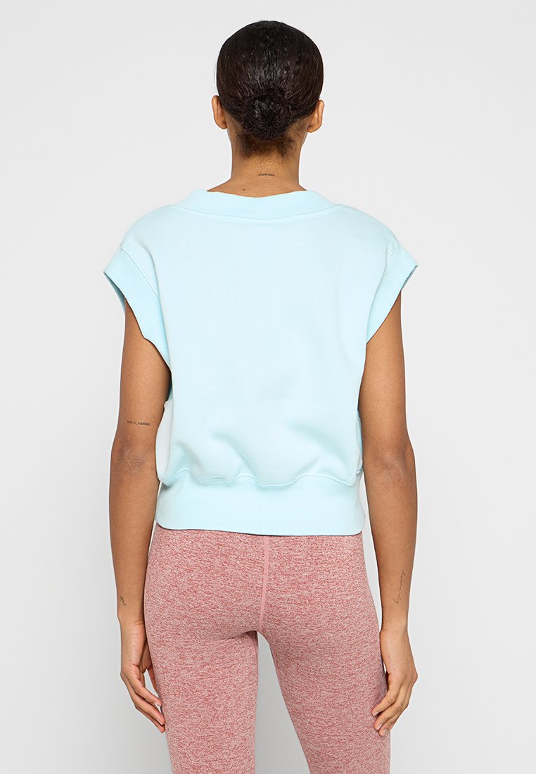 Sweat-shirt court bleu clair en tissu doux et lisse, avec des manches courtes et des détails côtelés à l'ourlet. Associé à des leggings roses.