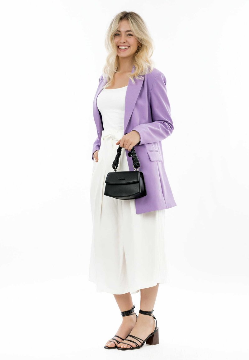 Blazer lila, blusa blanca y pantalones anchos blancos; bolso negro con un asa texturizada; tacones negros con tiras y tacón amplio.