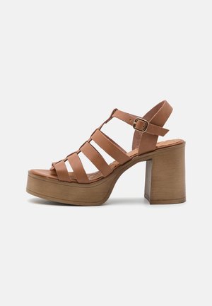 Brun læderplatformsandal med flere remme, en justerbar spænde og en chunky høj hæl på en lys baggrund.