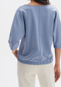 Top azzurro chiaro, dalla vestibilità ampia, realizzato in tessuto liscio. Maniche a tre quarti, orlo elasticizzato e dettagli con cucitura centrale sul retro.