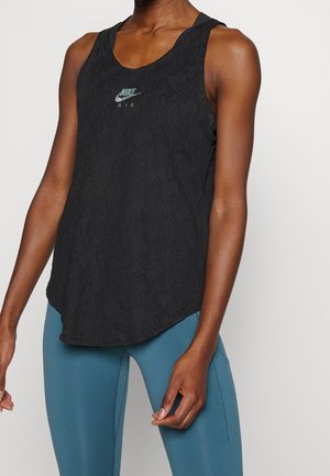 Osoba nosząca czarny bezrękawnik Nike Air z wypukłym napisem i niebieskie legginsy, stojąca na jednolitym tle.