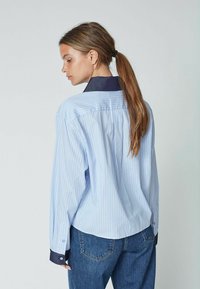 Cămașă cu dungi albastre și albe, cu guler și manșete marine, mâneci lungi, croi obișnuit și țesătură texturată. Purtați cu blugi din denim albastru.