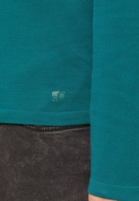 Błękitna koszula z długim rękawem o prążkowanej fakturze oraz subtelnym detalem logo w pobliżu brzegu, zestawiona z ciemnym dżinsowym materiałem.