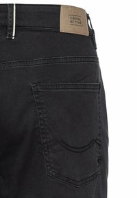 Zwarte denim jeans met een gestructureerde afwerking, voorzien van een bruine leren patch, zichtbare stiksels en een klassiek zakontwerp.