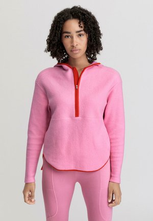 Pullover in pile rosa con colletto zip rosso e cappuccio. Presenta maniche lunghe e orlo inferiore arrotondato. Tessuto testurizzato.